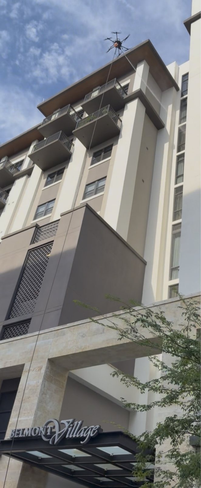 A Vista cleaning drone hovering above Belmont Village Senior Living in Coral Gables, its tether running down the facade to the coral stone entrance
