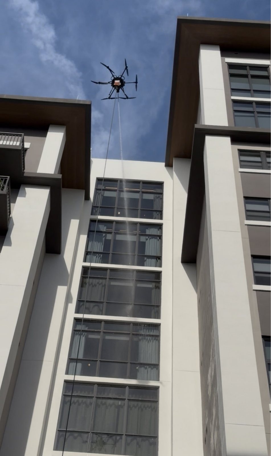 A tethered Vista cleaning drone above the Belmont Village courtyard, washing the glass line by line