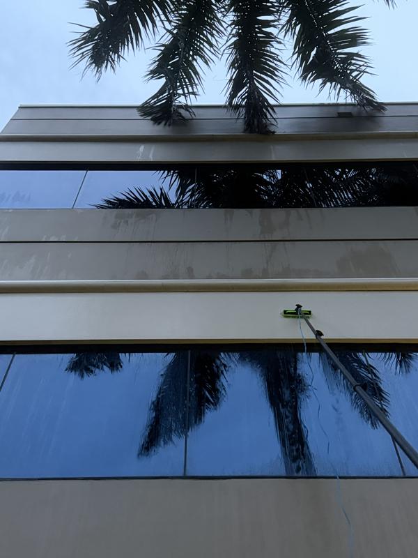 The water-fed pole brush working the glass beneath the algae-streaked panel bands