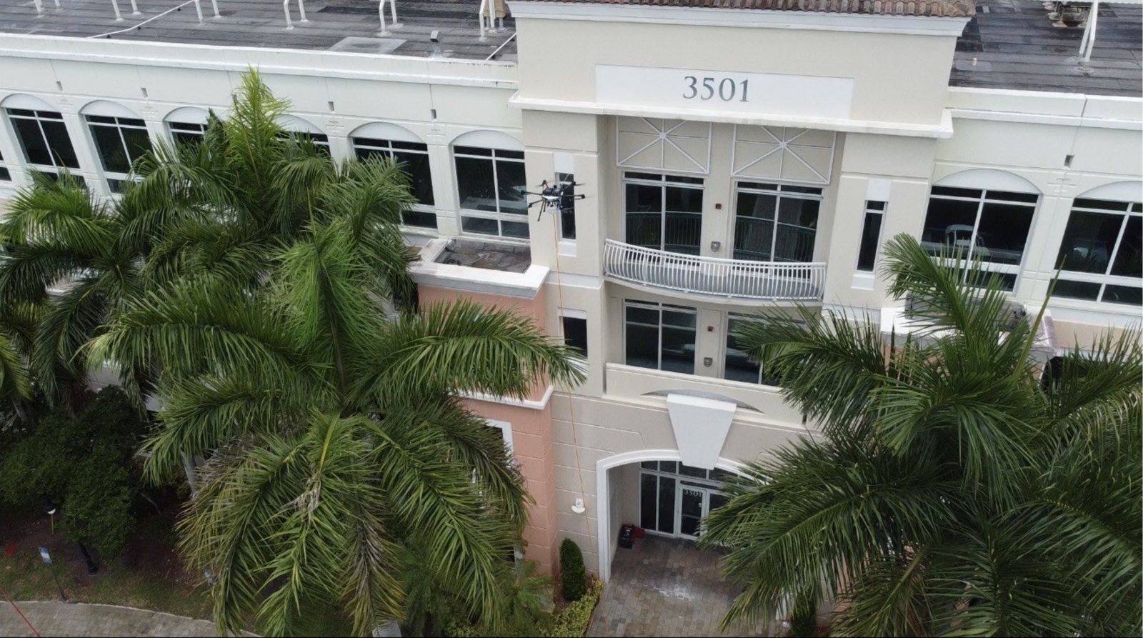A Vista cleaning drone working the facade of the 3501 tower at Miramar Centre II, framed by palms