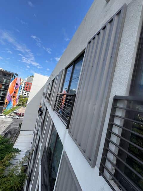 A Vista rope access technician on the facade of Sentral Wynwood, with Wynwood murals across the street